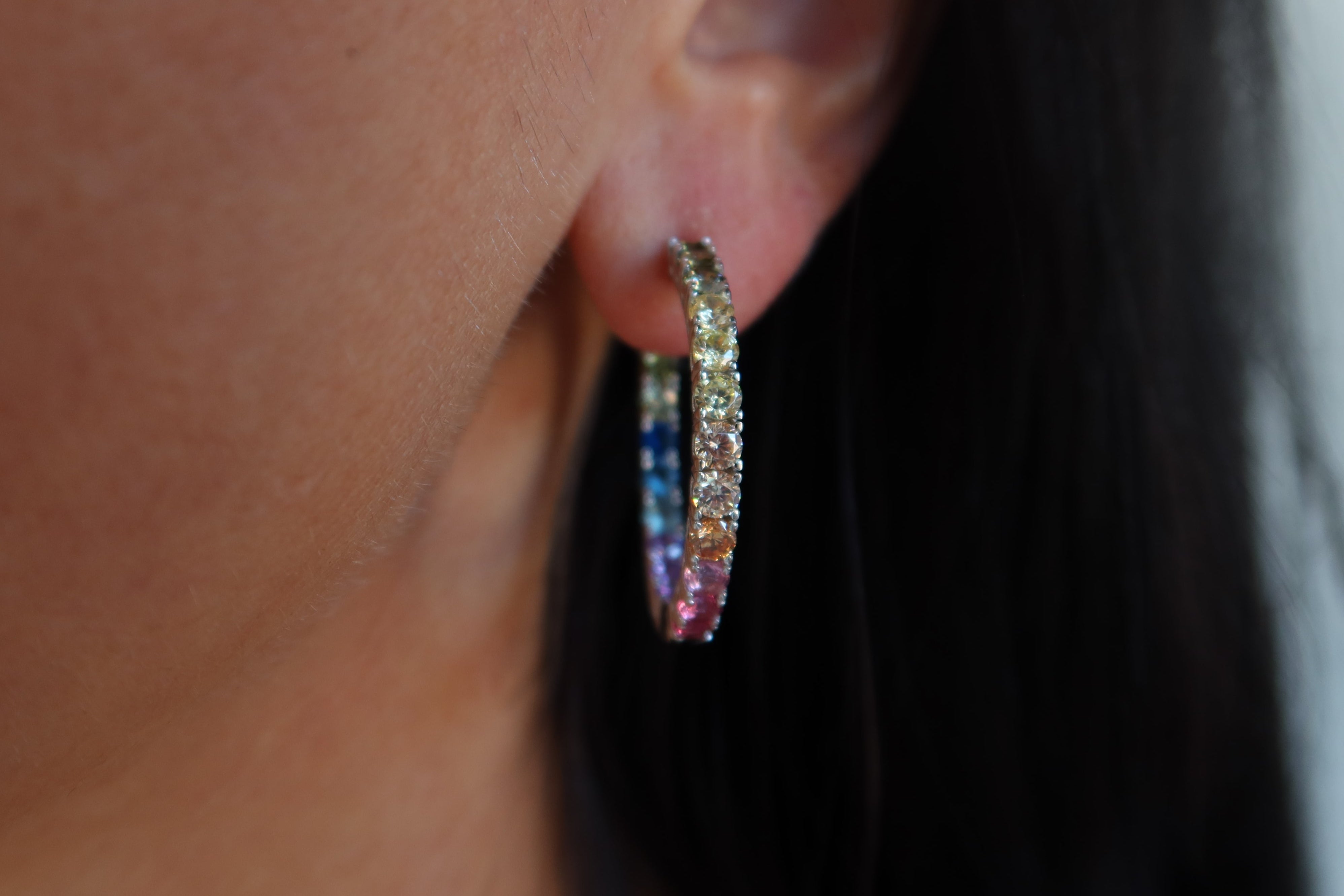 Close-up of an ear wearing a colorful hoop earring with blurred background